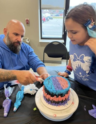 A Picture of an Adult with Child Decorating Cake
